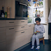 Un enfant mange un yogourth devant le frigo ouvert