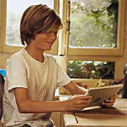 Un ado, assis à la cuisine, regarde sa tablette avec un sourire